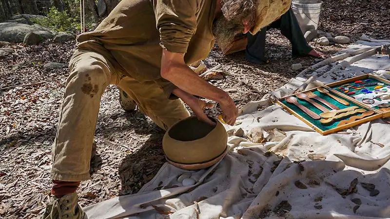 man knelt over a earthen clay pot he is making